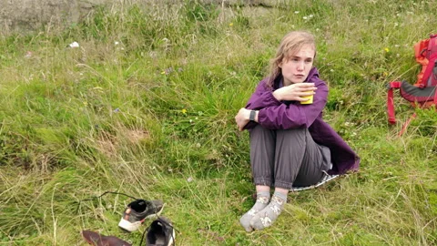 Female hiker sitting on grass drinking hot tea during hike break Stock Footage 340462672