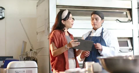 Female Hispanic manager holding tablet, pointing, African American chef in coat Stock Footage 339559751