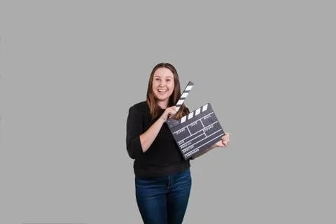 Female holding clapperboard smiling on solid gray background Stock Photos