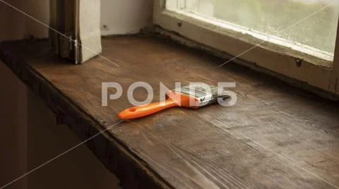 Female holding with a orange brush and painting windowsill with fresh varnish Stock Photos
