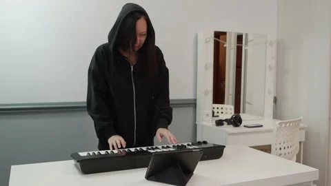 Female in hoodie practicing keyboard using tablet in lively studio scene Stock Footage 331983268