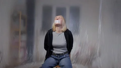 A female hostage is crying while sitting on a chair in an empty room Stock Footage 141585557