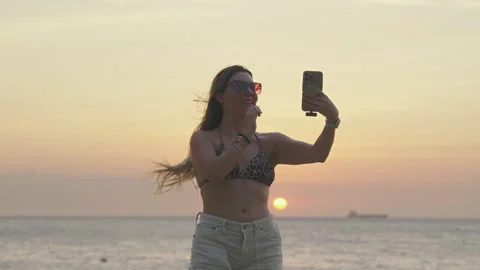 Female Influencer Talks To Mobile Camera On The Beach At Orange Sunset. - slow Stock Footage 331404505