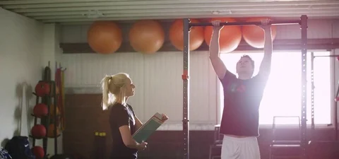 Female instructor assisting man with pull-up at gym 動画素材 78202506