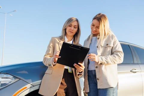 Female instructor explaining driving test details to learner driver near car Stock Photos