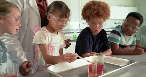 Female instructor in lab coat guiding girl using pipette transferring red liquid Stock Footage 341467742