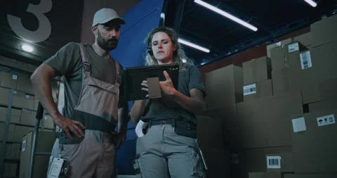 Female Inventory Specialist Using Tablet Computer, Loader Checking Cardboard Stock Footage 313346892