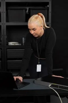 Female IT network technician in her twenties reviewing laptop beside network Stock Photos