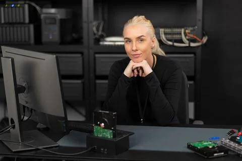 Female IT security technician in a server room at a desk with storage equipment Stockfoto's