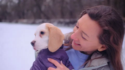 Female in jacket hugs with cute beagle puppy on the snowy bank near a frozen riv Stock Footage 169636053