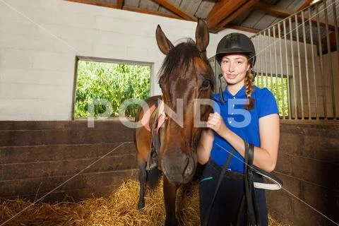 Female jockey standing in stable with bay horse Stock Photos