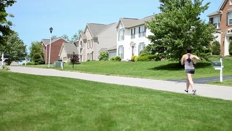 Female Jogger runs up residential road in planned suburban neighborhood Stock Footage