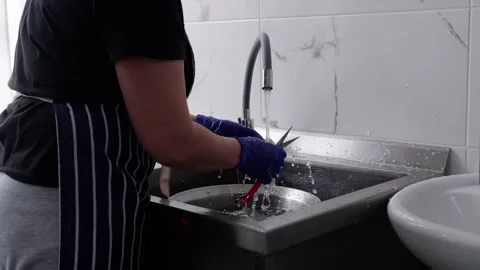Female kitchen worker wearing blue gloves cuts vegetables with scissors over a Stock Footage 336063657