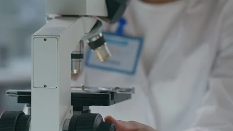 Female Lab Scientist Using Focus Knob as Looking through Microscope Stock Footage 304764300