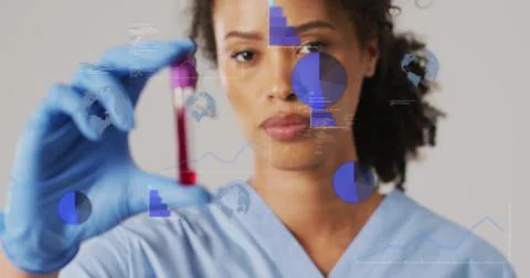 Female lab-tech checking blood vial with purple cap in lab, blue scrubs, blue Stock Photos