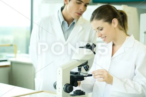 Female Lab Worker Placing Slide Under Microscope, Male Colleague Looking Over