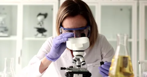 Female lab worker pours sample of reagent on microscope stage Stock Footage 285662150