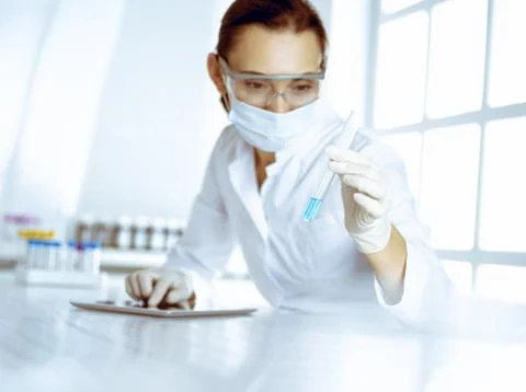 Female laboratory assistant analyzing test tube with blue liquid. Medicine Stock Photos