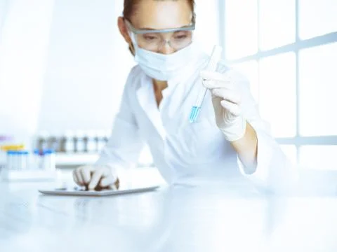 Female laboratory assistant analyzing test tube with blue liquid. Medicine Stock Photos