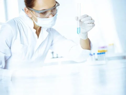 Female laboratory assistant analyzing test tube with blue liquid. Medicine Stock Photos