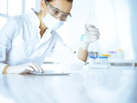 Female laboratory assistant analyzing test tube with blue liquid. Medicine Stock Photos