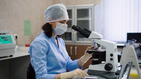 Female laboratory worker using microscope. Young female specialist in uniform Stock Footage 74596856