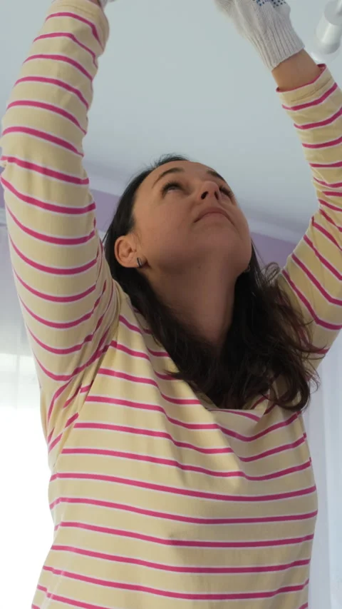 Female on ladder fixing ceiling light fixture Stock Footage 318274130