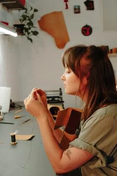 Female leatherworker prepares thread while seated at a craft bench with leather Stock Photos