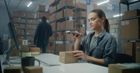 Female logistics manager scans parcel using smartphone, enters information on 스톡 동영상 307618510