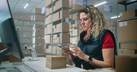 Female logistics manager scans small parcels using smartphone, works in 動画素材 307558247