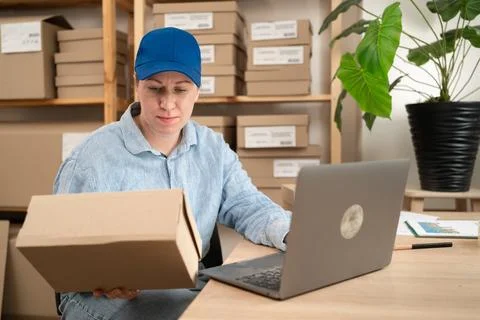 Female logistics worker using laptop computer in parcel warehouse while manag Stock Photos