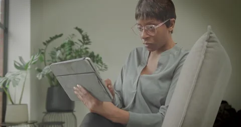 Female Looking at Chart on Digital Tablet, Sitting on Sofa Working at Home Stock Footage 173439513