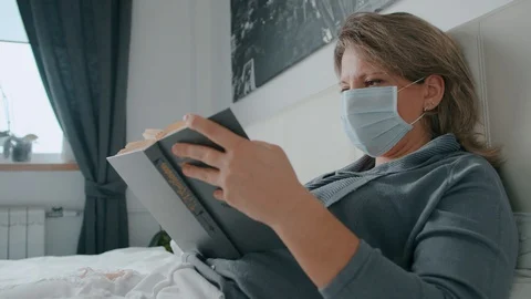 Female lying on bed sick and reading a book and sneezes coronavirus Stock Footage 130084172