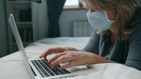 Female lying on bed working with laptop in mask coronavirus Stock Footage 130084258