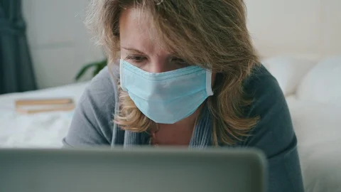 Female lying on bed working with laptop in mask coronavirus Stock Footage 130084261