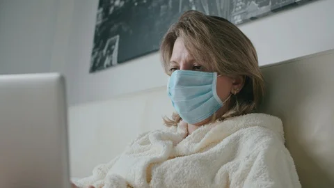 Female lying on bed working with laptop in mask coronavirus Stock Footage 130084262