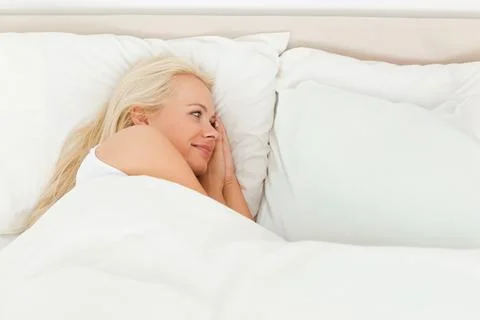 Female lying on right side in bed on stacked pillows, wearing white tank top, Stock Photos