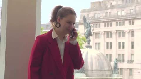 Female Manager in Red Jacket Talks on Phone at Window with Derby Square View Stock Footage 333313560
