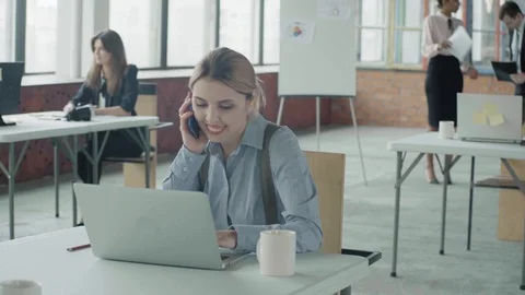 A female manager is sitting at a table with a laptop and talking on the phone Stock Footage 124273382