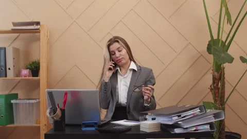 Female manager takes off glasses while talking to client on smartphone while Stock Footage 196883198