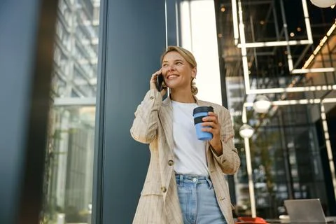 Female manager talking phone while drinking coffee standing on modern office Stock Photos