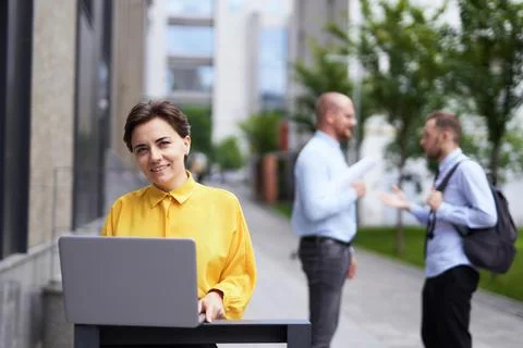 Female manager using laptop outdoor, two men on background Stock-Fotos