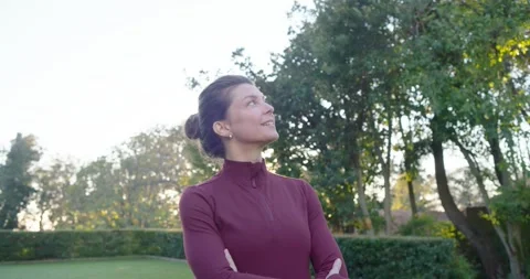 Female in maroon pullover standing on manicured lawn, tracking low sun while Stock Footage 342031667