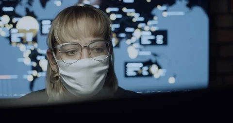 Female in mask working on computer, coronavirus pandemic. World map live counter Stock Footage 129039748