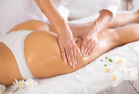 Female masseur performs stroking during spa procedure of thigh area for girl Stock Photos