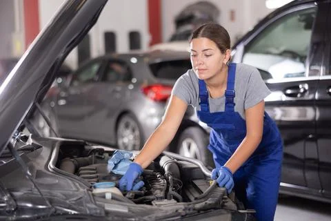 Female mechanic adjusting engine under hood of vehicle in workshop 스톡 사진