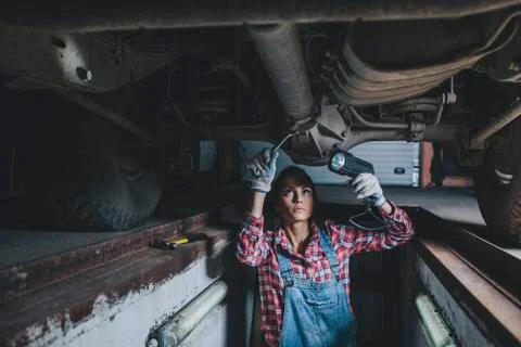Female mechanic holding flashlight while working underneath car at workshop Stock Photos