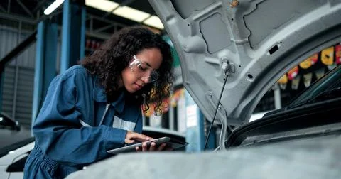 Female mechanic using tablet with diagnostics software checking car engine Foto stock