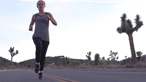 Female model running toward camera on desert road at sunset Stockbeeldmateriaal 76722414