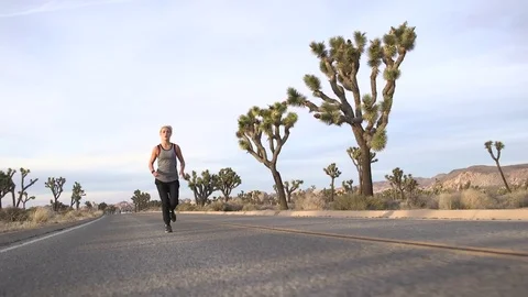 Female model running toward camera on desert road at sunset 스톡 동영상 76722560